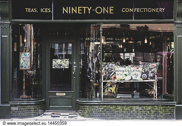 Exterior view of interior design store with floral print cushions on vintage metal bench in shop window.