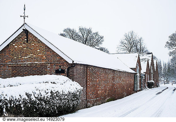 Exterior view of red brick cottages with snow-covered roofs along a rural road.