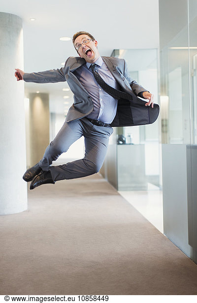 Exuberant businessman jumping for joy in office corridor