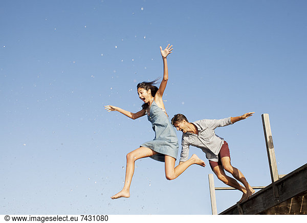 Exuberant couple jumping off dock