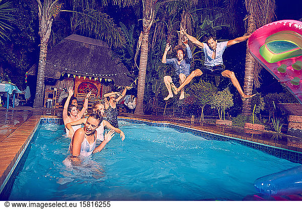 Exuberant young men friends jumping into swimming pool at night
