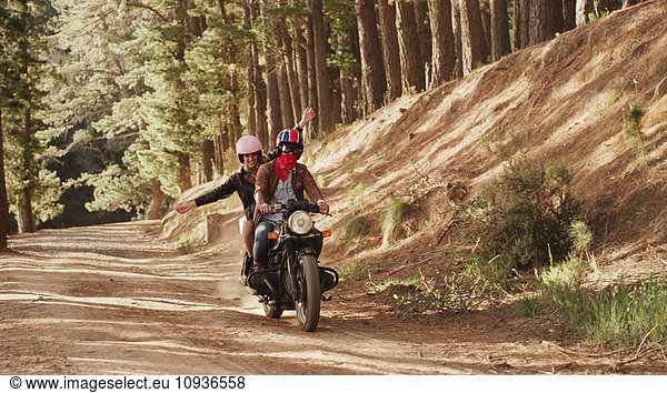 Exuberant young woman riding motorcycle on dirt road in woods