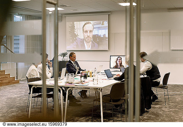 Führungskräfte aus der Wirtschaft diskutieren in einer Sitzung während einer Webkonferenz durch Glas im Büro gesehen