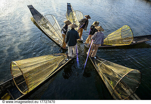 Fünf Fischer auf traditionellen Booten mit konischen Netzen.