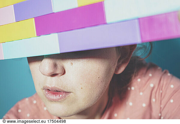 Face of adult woman hiding eyes behind toy blocks