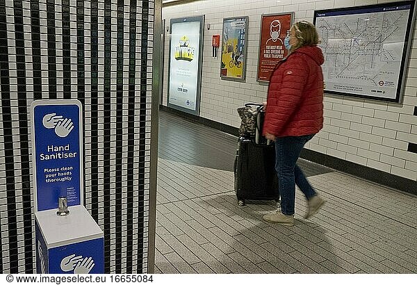 Fahrgäste in einer Londoner U-Bahn-Station mit Händedesinfektionsmitteln und Schildern  die aufgrund der Coronavirus-/Covid-19-Pandemie in London  England  Vereinigtes Königreich  auf einen sicheren Sicherheitsabstand hinweisen.