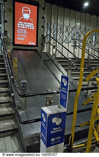 Fahrgäste in einer Londoner U-Bahn-Station mit Händedesinfektionsmitteln und Schildern  die aufgrund der Coronavirus-/Covid-19-Pandemie in London  England  Vereinigtes Königreich  auf einen sicheren Sicherheitsabstand hinweisen.