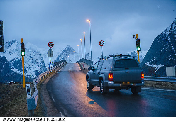 Fahrzeug überquert grüne Ampelbrücke bei Dämmerung  Reine  Lofoten  Norwegen