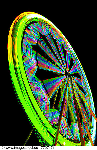 Fairground ferrish wheel with lights in rainbow colours  against a black sky.