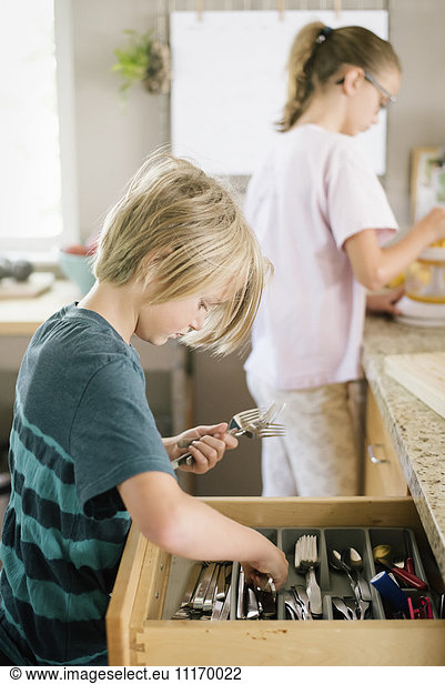 Familie bereitet das Frühstück in einer Küche vor  Junge holt Besteck aus einer Schublade.