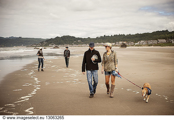 Familie mit Haustier geht am Strand vor bewölktem Himmel spazieren