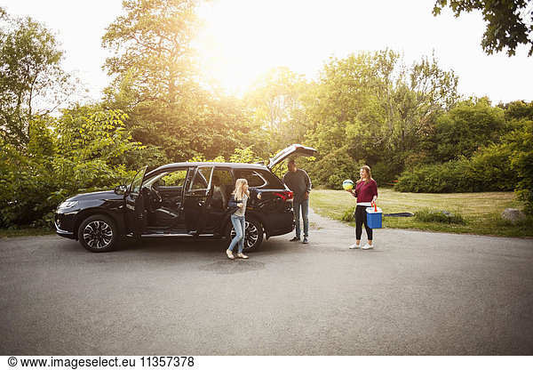 Familie mit schwarzem Elektroauto gegen Bäume im Park