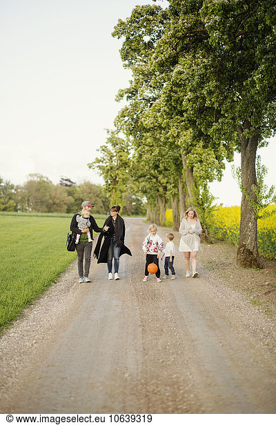 Family and friends walking on dirt road by oilseed rape field