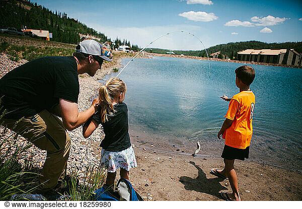 Family catches a fish from a mountain lake on adventure vacation
