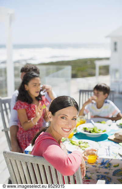 Family eating lunch at table on sunny patio overlooking ocean