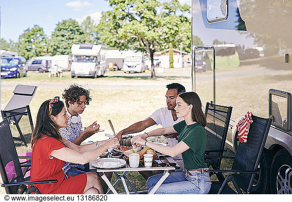 Family enjoying food at table while sitting outside camper van in trailer park