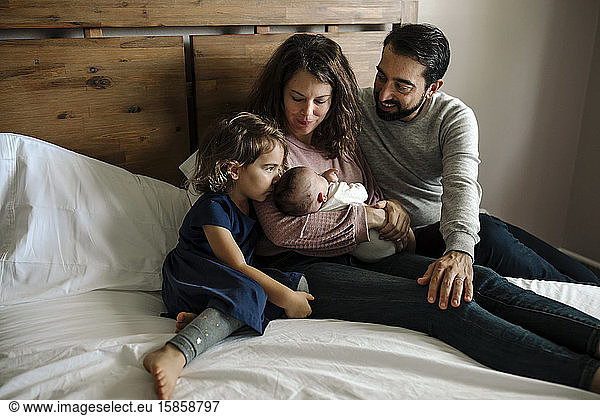 Family gathered in bed with wood headboard admiring newborn baby