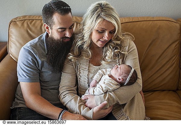 Family holding sleeping newborn daughter on couch at home