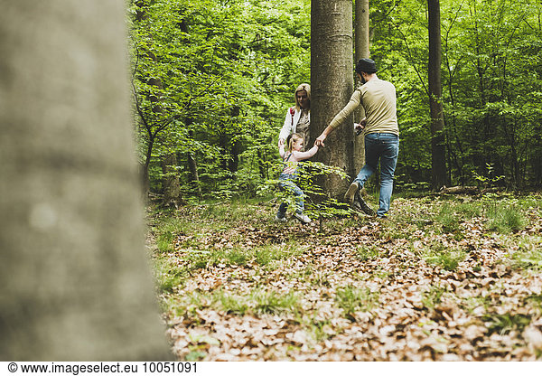 Family in forest running around tree trunk