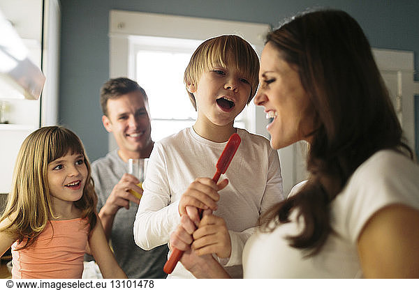 Family looking at woman singing with spatula in kitchen