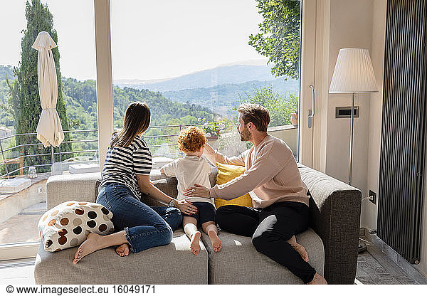 Family looking out through window while sitting on sofa in living room at home