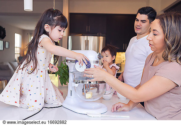Family of 4 in the kitchen,  mom helping older daughter bake cookies.