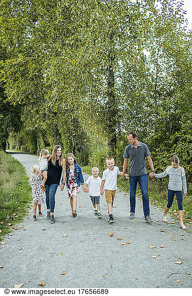 Family of eight  hold hands walking oathway at nature park.
