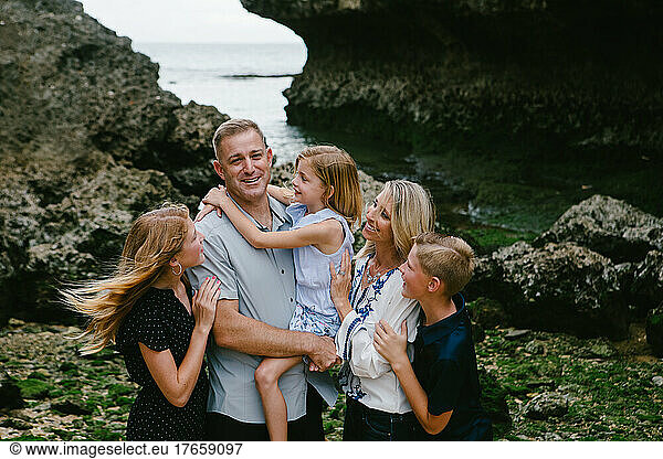 Family of five hugs and laughs together on tropical beach