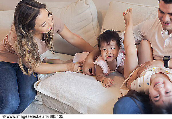 Family of four playing tickle fight on the couch at home.