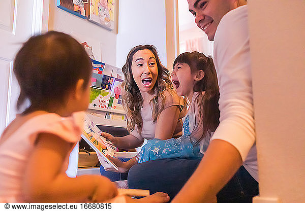 Family of four sitting on the floor and reading children's books.