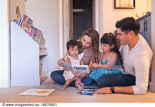 Family of four sitting on the floor and reading children's books.