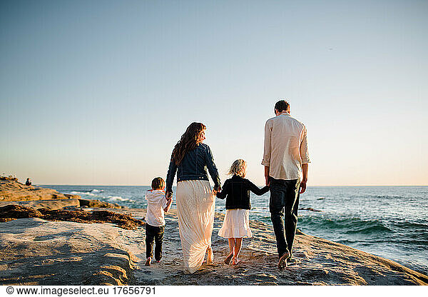 Family of Four Walking Along Cliff on Beach at Sunset in San Diego