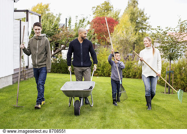 Family of four with gardening equipment walking in yard
