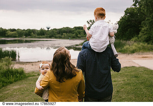 Family of four with red hair walks by lake with green trees