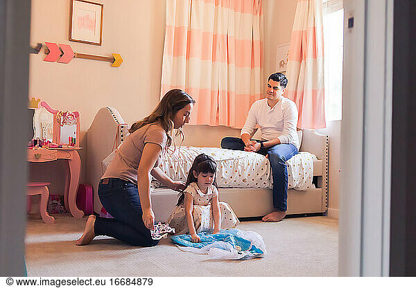 Family of three in daughter's bedroom picking out a princess dress.