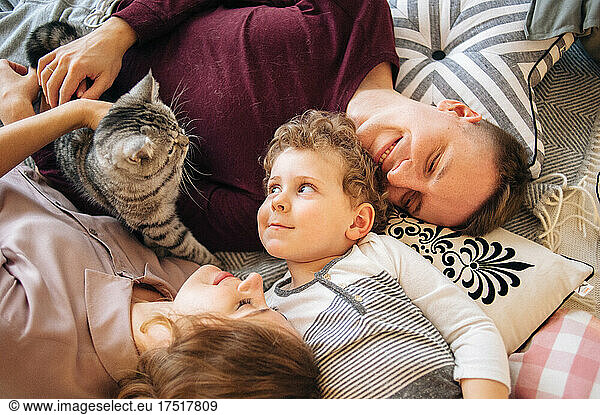 Family of three lay on bed and have fun with cat