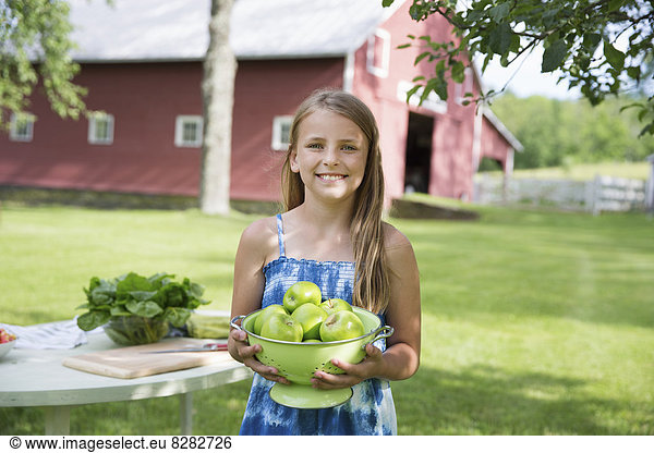 Family Party. A Young Girl With Long Blonde Hair Wearing A Blue Sundress  Carrying A Large Bowl Of Crisp Green Skinned Apples.