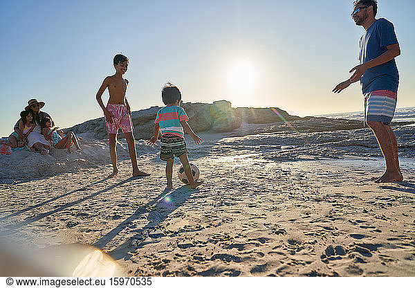 Family playing soccer on sunny beach