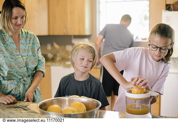 Family preparing breakfast in a kitchen  girl squeezing oranges.
