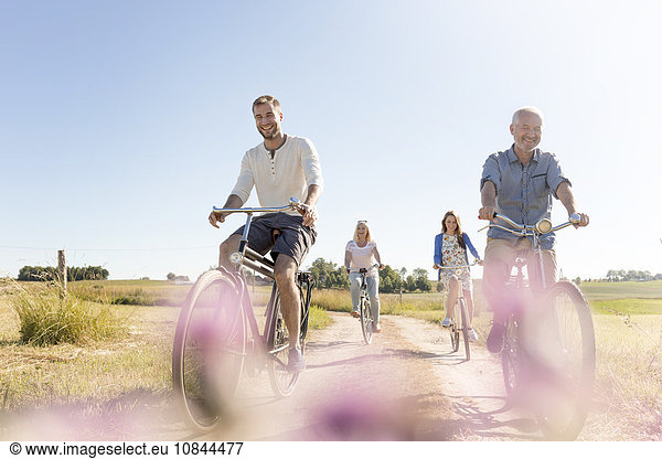 Family riding bicycles on sunny rural dirt road