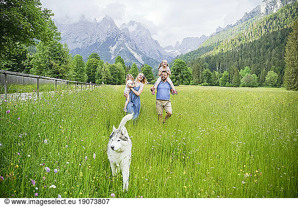 Family spending vacation with dog walking on grass in front of mountains