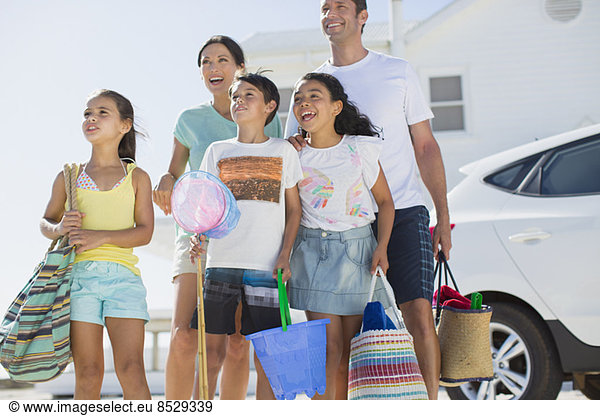 Family standing with beach gear in sunny driveway