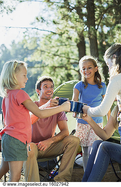 Family toasting mugs at campsite in woods