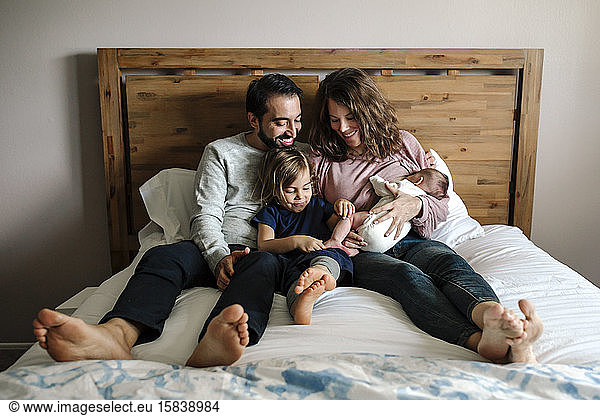 Family together on bed as dad holds 4 yr old and mom nurses newborn