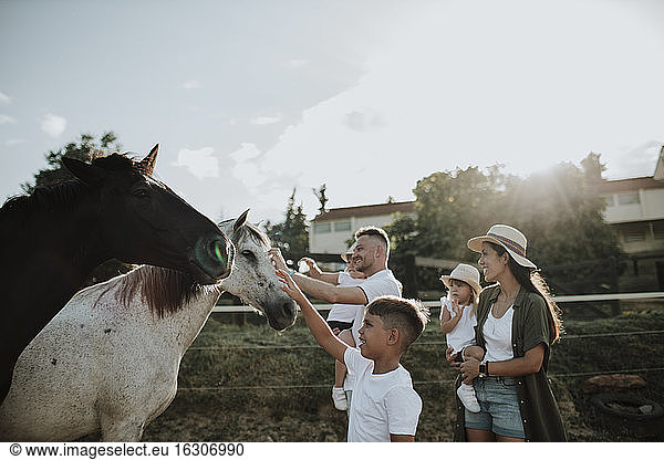 Family touching horses while standing against sky