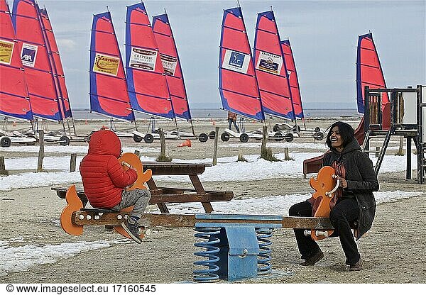 Family under the winter cold of a playground in Mont St Michel bay with snow  Hirel  Brittany  France.