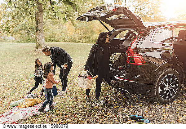 Family unloading luggage from electric car on field during picnic