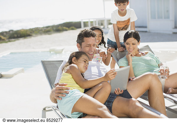 Family using digital tablet on lounge chair at poolside