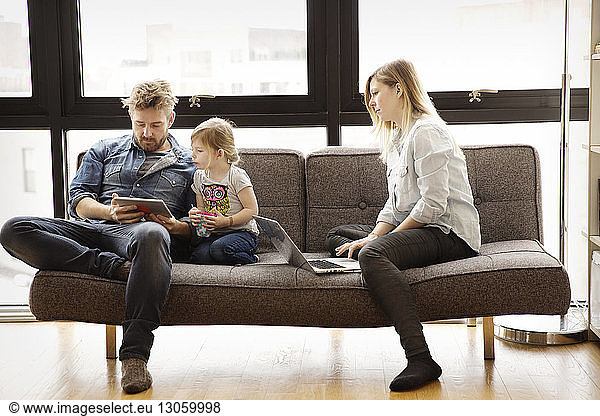 Family using technologies while sitting on sofa at home