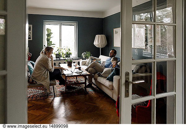 Family using various technologies in living room seen through doorway at home